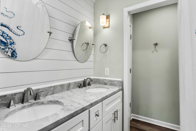 bathroom featuring oversized vanity, wood walls, hardwood / wood-style flooring, and dual sinks