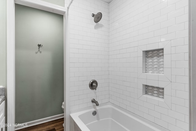 bathroom featuring tiled shower / bath combo, hardwood / wood-style floors, and toilet