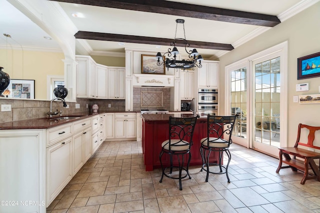 kitchen with a chandelier, tasteful backsplash, pendant lighting, sink, and beam ceiling