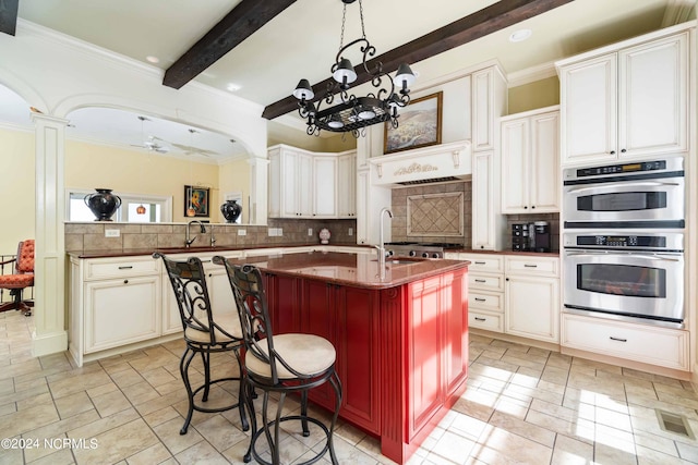 kitchen with backsplash, stainless steel double oven, beamed ceiling, and decorative columns