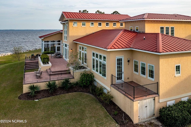 rear view of house featuring a deck with water view, a lawn, and a patio area