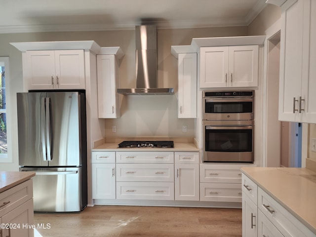 kitchen featuring white cabinets, appliances with stainless steel finishes, ornamental molding, and wall chimney exhaust hood