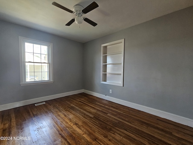 empty room featuring built in features, dark wood-type flooring, and ceiling fan