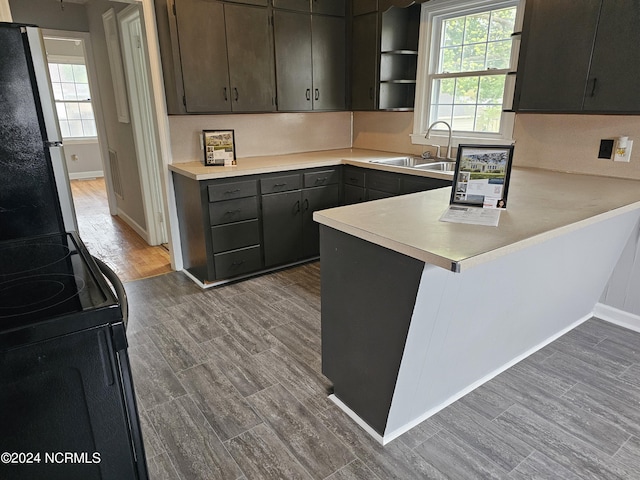 kitchen featuring sink, light wood-type flooring, a healthy amount of sunlight, kitchen peninsula, and stainless steel refrigerator