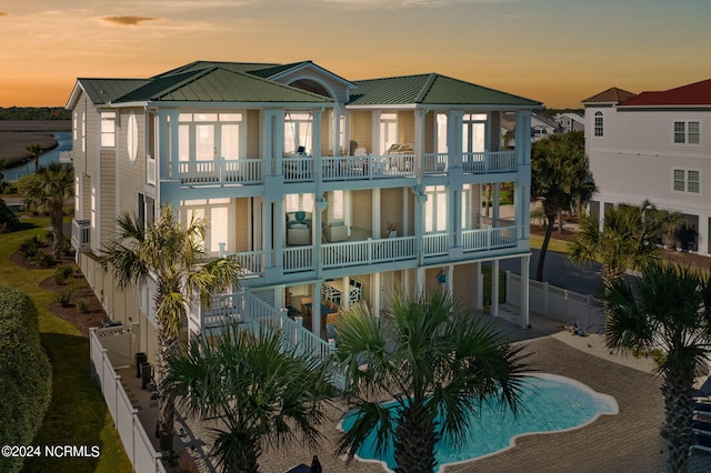 back house at dusk featuring a balcony and a fenced in pool