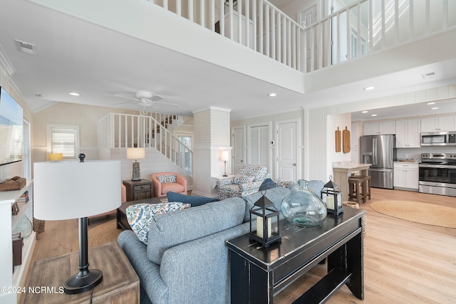 living room with light wood-type flooring, a towering ceiling, and ceiling fan