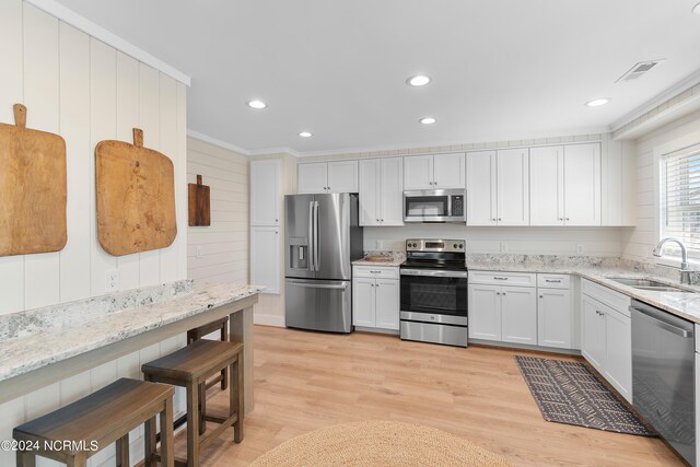 kitchen featuring ornamental molding, stainless steel appliances, light stone counters, sink, and light hardwood / wood-style floors