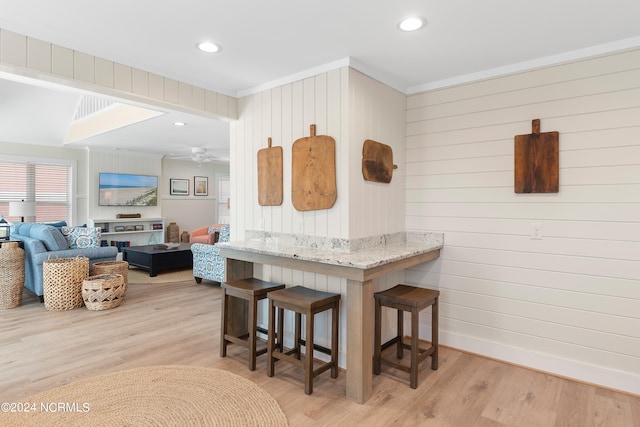 kitchen featuring a breakfast bar, wood walls, ceiling fan, and light hardwood / wood-style floors