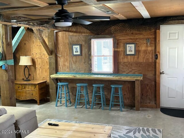 bar featuring concrete floors, ceiling fan, and wooden walls