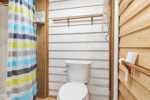 bathroom featuring curtained shower, wooden walls, and toilet