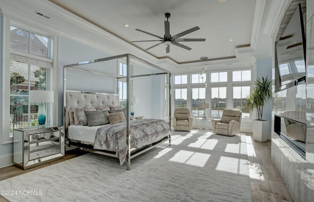 bedroom featuring multiple windows, light hardwood / wood-style floors, a high ceiling, and a tray ceiling