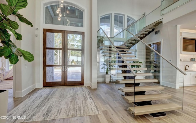 foyer featuring french doors, light wood-type flooring, a high ceiling, and plenty of natural light