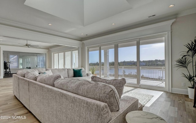 living room with light hardwood / wood-style flooring, a water view, ornamental molding, a raised ceiling, and ceiling fan