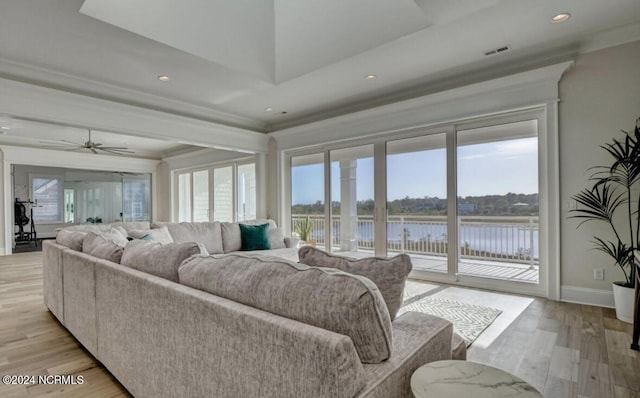 living room with crown molding, a water view, a raised ceiling, light hardwood / wood-style floors, and ceiling fan