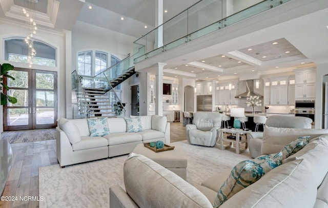 living room featuring french doors, light hardwood / wood-style flooring, crown molding, a high ceiling, and ornate columns