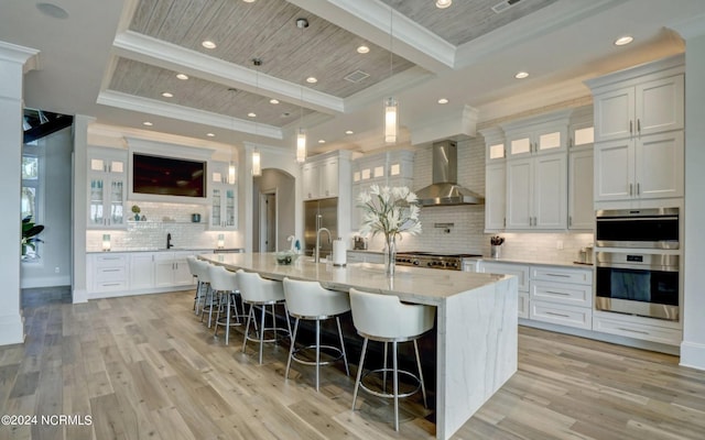 kitchen with an island with sink, beam ceiling, tasteful backsplash, and wall chimney exhaust hood