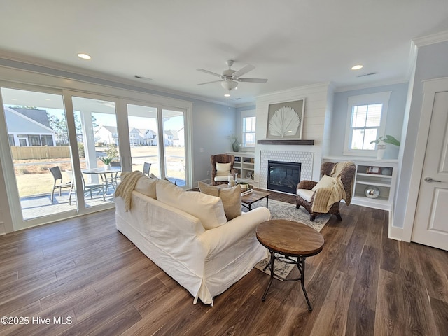 living area with a ceiling fan, dark wood-style floors, recessed lighting, ornamental molding, and a glass covered fireplace