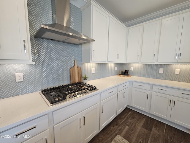 kitchen with dark wood-type flooring, wall chimney range hood, decorative backsplash, stainless steel gas stovetop, and white cabinetry