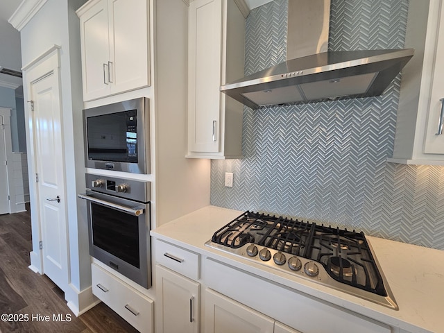 kitchen with appliances with stainless steel finishes, white cabinetry, dark hardwood / wood-style floors, decorative backsplash, and wall chimney exhaust hood