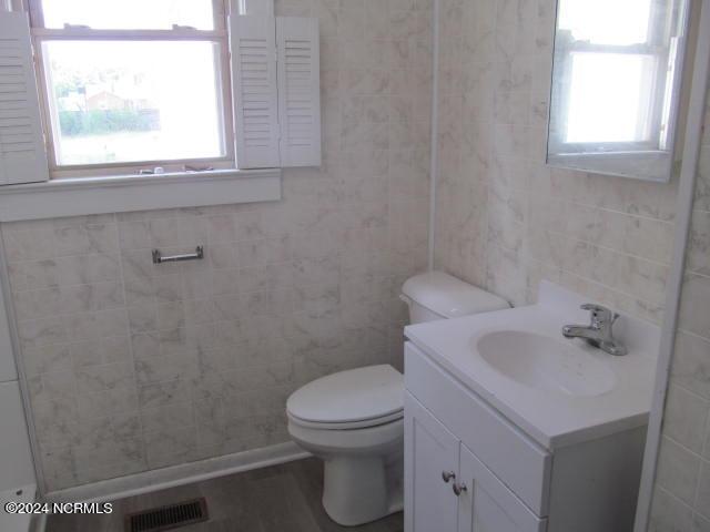 bathroom featuring vanity, toilet, and tile walls