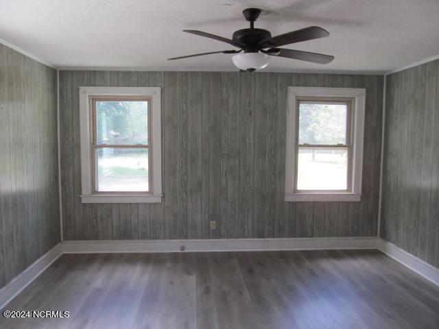 empty room with wood walls, ceiling fan, and hardwood / wood-style flooring