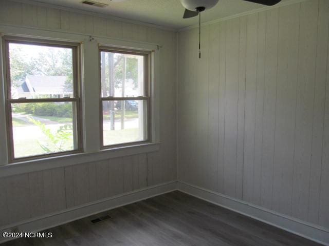 empty room featuring visible vents, dark wood-type flooring, baseboards, ornamental molding, and a ceiling fan