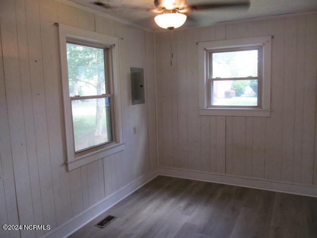 empty room with crown molding, electric panel, dark wood-type flooring, wood walls, and ceiling fan