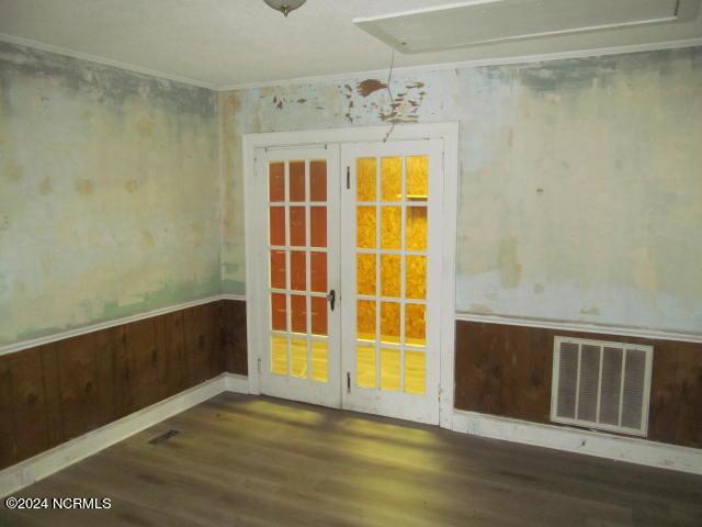 unfurnished room with wood finished floors, visible vents, french doors, wainscoting, and crown molding