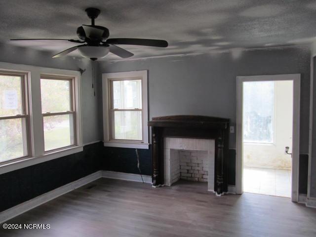 unfurnished living room featuring a ceiling fan, wood finished floors, baseboards, a fireplace, and a textured ceiling