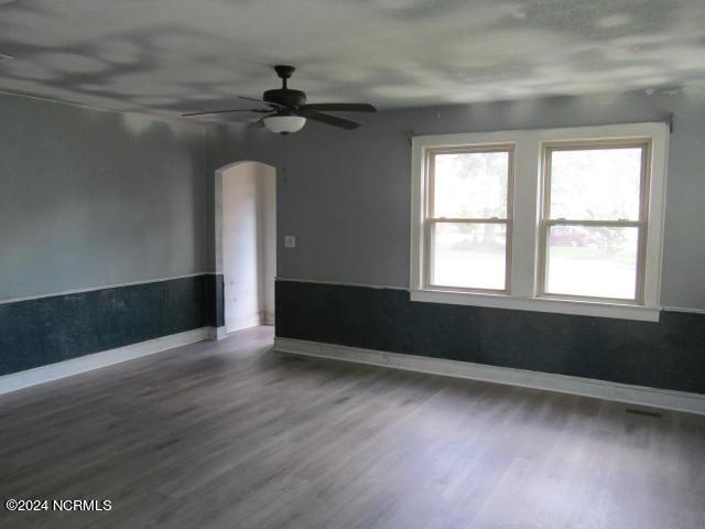 spare room with baseboards, arched walkways, wood finished floors, and a ceiling fan