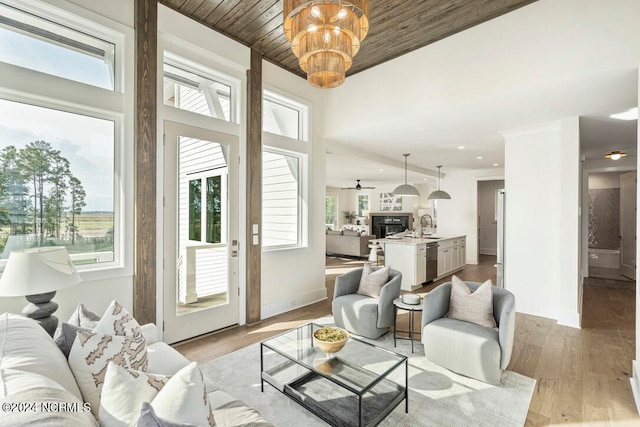 living room with a high ceiling, light wood-type flooring, ceiling fan, wood ceiling, and sink