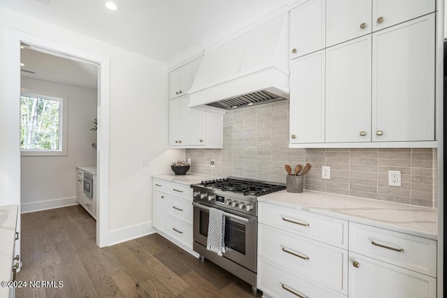 kitchen with dark wood-type flooring, stainless steel range with gas stovetop, light stone countertops, white cabinets, and custom exhaust hood