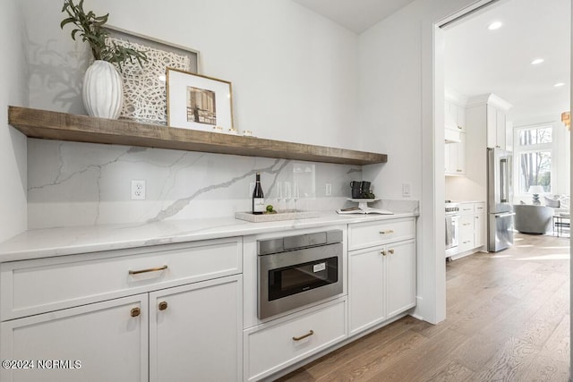 bar featuring stainless steel appliances, light stone countertops, white cabinets, decorative backsplash, and light wood-type flooring