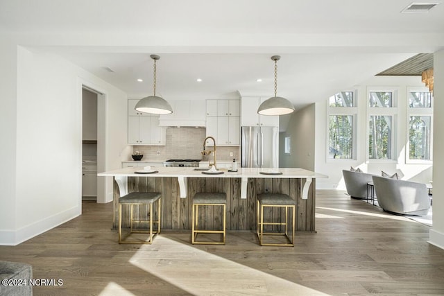 kitchen featuring decorative backsplash, stainless steel fridge, hanging light fixtures, and a large island with sink