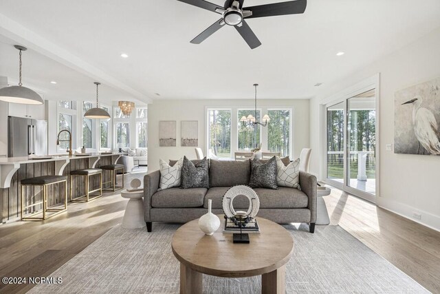 living room featuring ceiling fan with notable chandelier, light hardwood / wood-style floors, and a healthy amount of sunlight