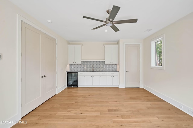 kitchen with tasteful backsplash, beverage cooler, light wood-type flooring, and white cabinets