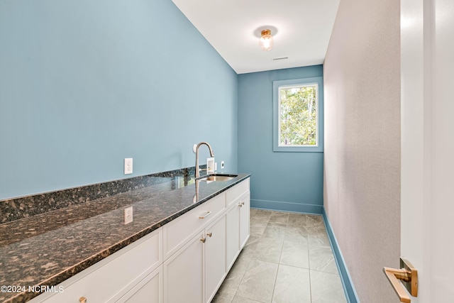 interior space with light tile patterned floors, dark stone countertops, sink, and white cabinets