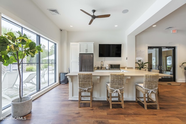 kitchen featuring ceiling fan, white cabinetry, stainless steel refrigerator, dark hardwood / wood-style floors, and a breakfast bar area