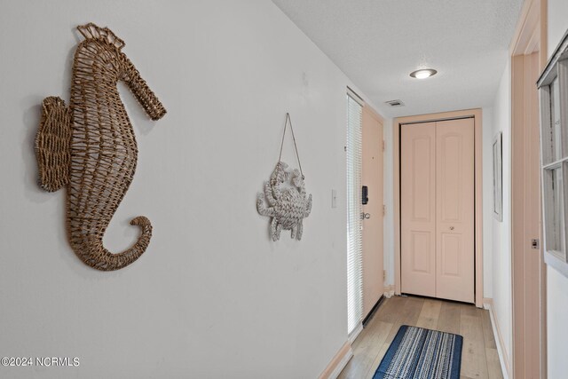 corridor with a textured ceiling and light wood-type flooring