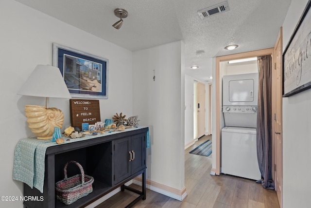 corridor featuring stacked washer and dryer, wood-type flooring, and a textured ceiling