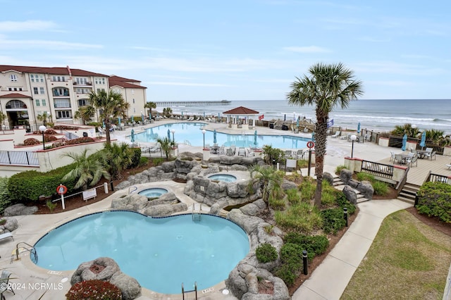 view of pool with a water view, a patio area, and a community hot tub