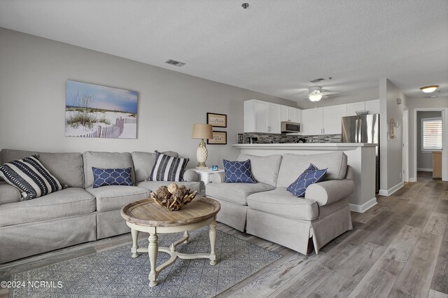 living room featuring ceiling fan, light hardwood / wood-style flooring, and a textured ceiling