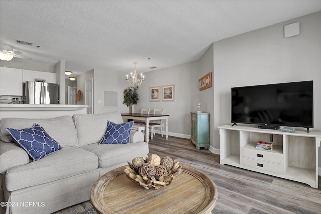 living room with hardwood / wood-style flooring, ceiling fan with notable chandelier, and a textured ceiling