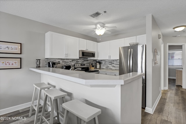 kitchen featuring appliances with stainless steel finishes, backsplash, a kitchen breakfast bar, white cabinets, and kitchen peninsula