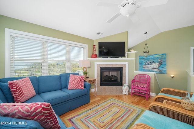 living room featuring vaulted ceiling, a tile fireplace, ceiling fan, and light wood-type flooring