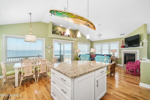 kitchen with light stone counters, hanging light fixtures, a kitchen island, light hardwood / wood-style floors, and white cabinets