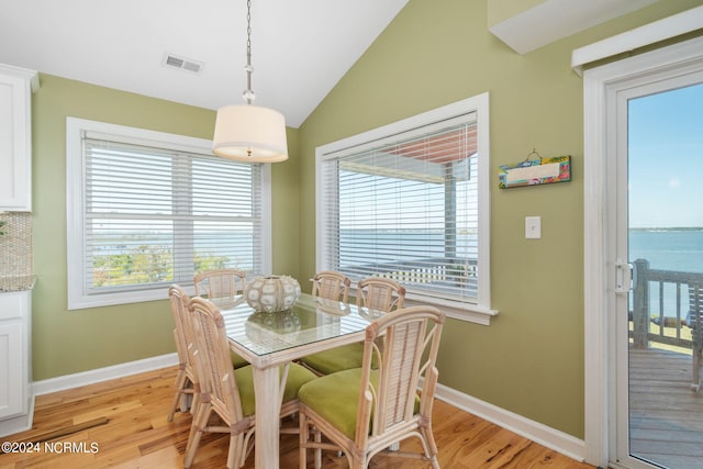 dining space with light hardwood / wood-style flooring, plenty of natural light, vaulted ceiling, and a water view