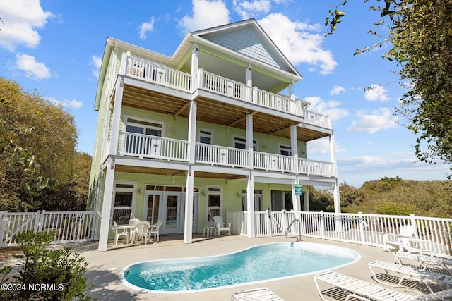 rear view of property with a balcony, a fenced in pool, a patio area, and french doors