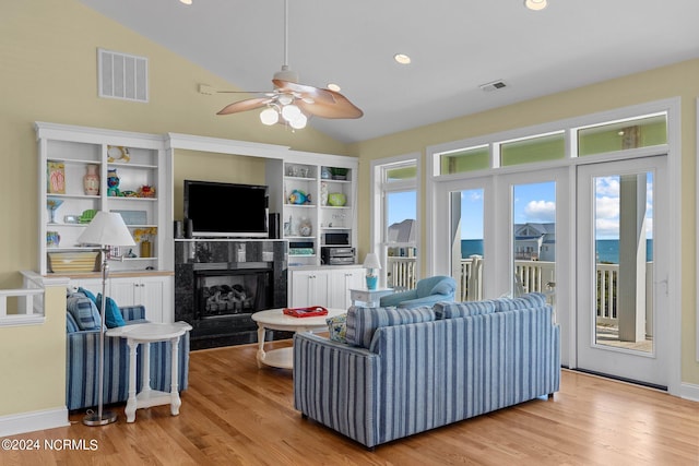 living room featuring a water view, lofted ceiling, ceiling fan, a premium fireplace, and light hardwood / wood-style floors