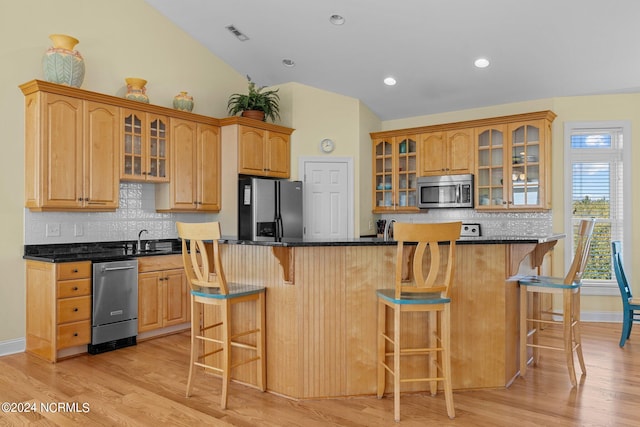 kitchen featuring appliances with stainless steel finishes, tasteful backsplash, light hardwood / wood-style floors, a kitchen bar, and a center island